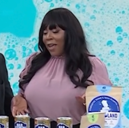 Woman standing behind a table with cans and a package, against a blue bubble-patterned background