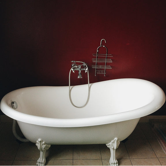 White clawfoot bathtub with a silver faucet and hanging metal shower caddy against a dark red wall.