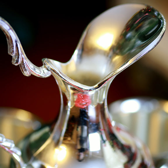 Close-up view of a shiny silver pitcher with a curved spout and decorative handle.