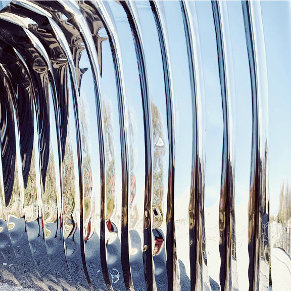 Close-up of shiny metallic vertical bars reflecting a distorted outdoor scene with trees and sky.