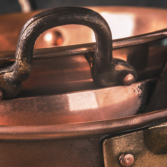 Close-up of metal handles on stacked copper pots with a warm light reflection.