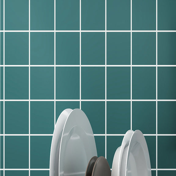 White plates and a dark bowl drying on a rack in front of a green tiled wall with white grout.